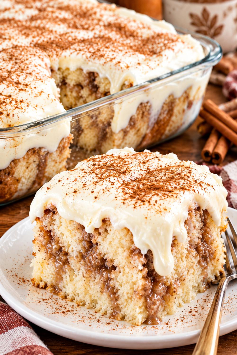 Cinnamon roll poke cake slice with cream cheese frosting and a dusting of cinnamon on a plate